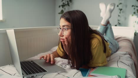 adolescente caucásica acostada en la cama en el frente y haciendo la tarea
