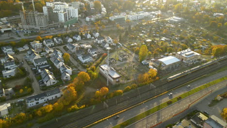 aerial following passenger train moving on railroad in autumn through urban district of gdynia city at sunrise - top view