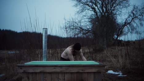 shirtless man is going to bathe on outdoor tub heated by firewood