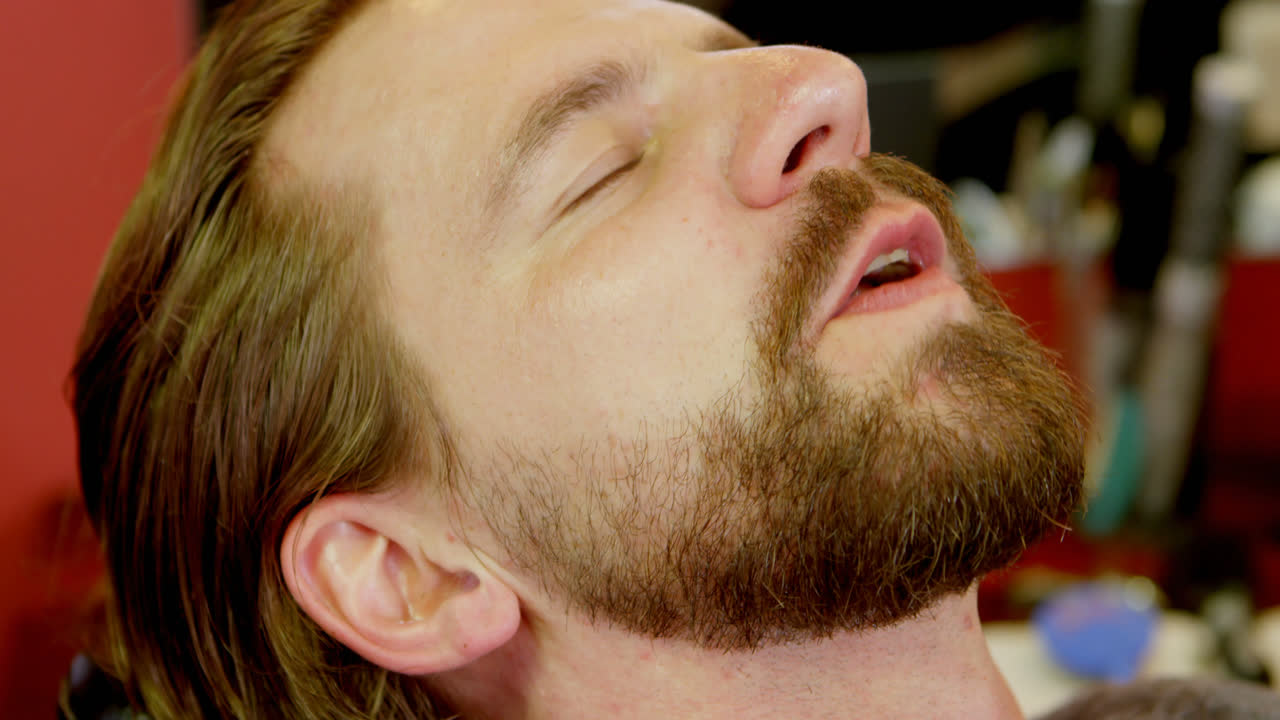 el barbero está arreglando la barba del hombre en la barbería 4k