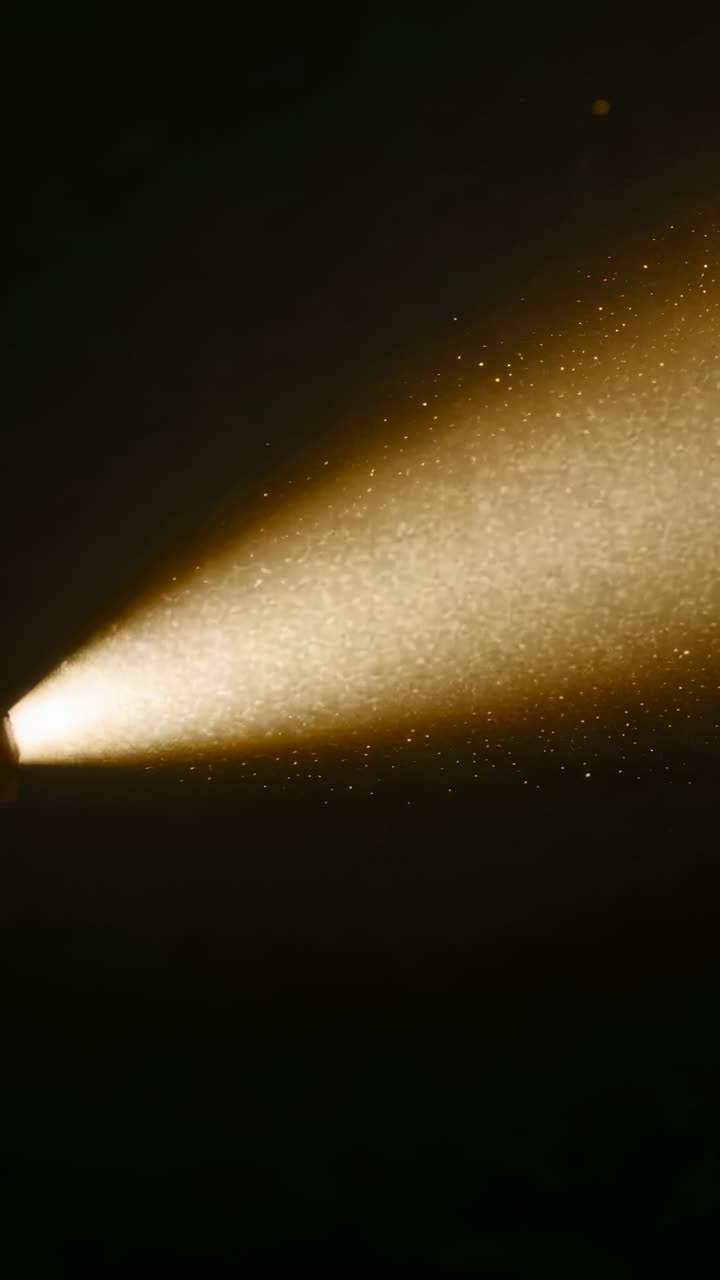 Vertical video: Starting spotlight projecting golden beam in dark studio, revealing dust motes