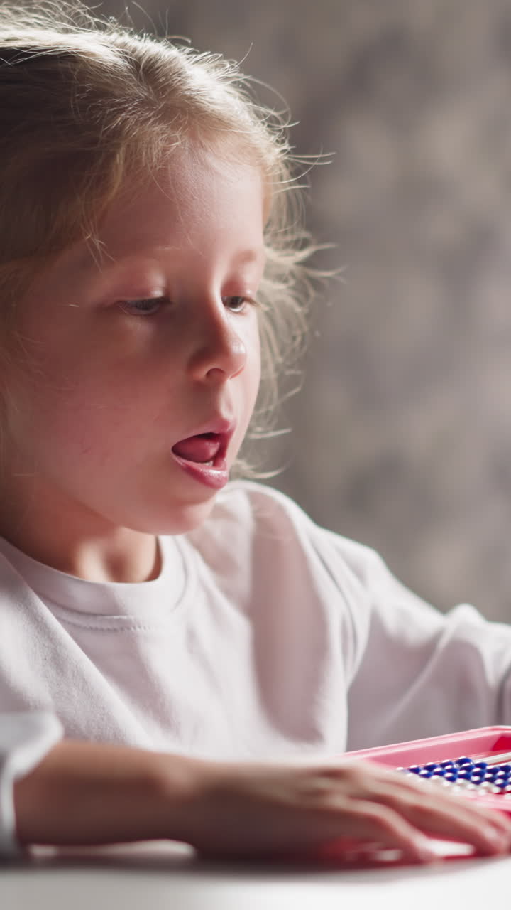 Thoughtful little girl student plays with colorful plastic abacus sitting at table during mental maths lesson in children room closeup slow motion