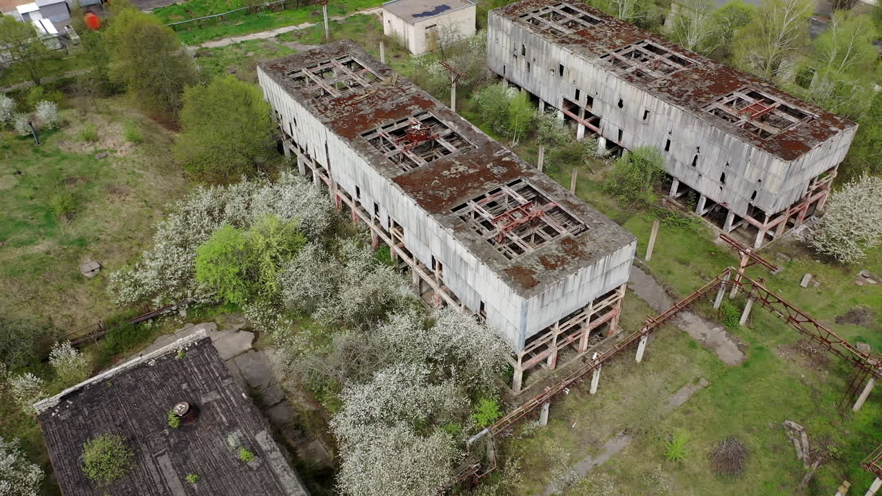 Destroyed factory buildings with holes in roofs. Old abandoned industrial plant. Ruined manufacturing on green nature background. View from above.