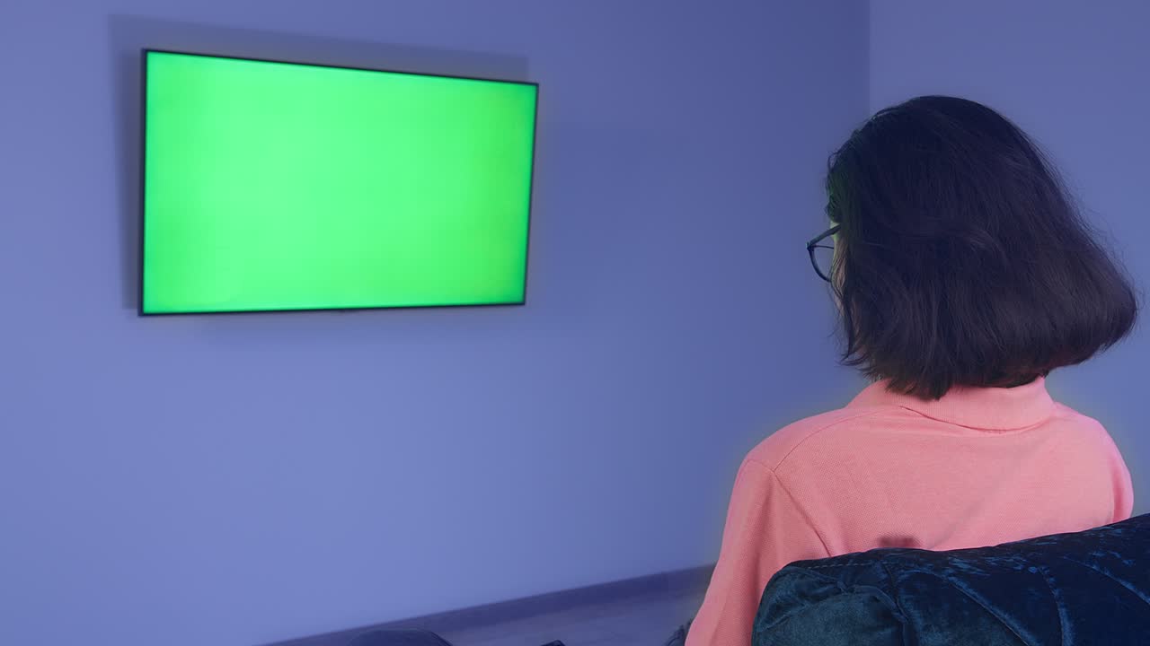 chica sentada frente a una televisión colgada en la pared, viendo las noticias, chromakey, vista trasera