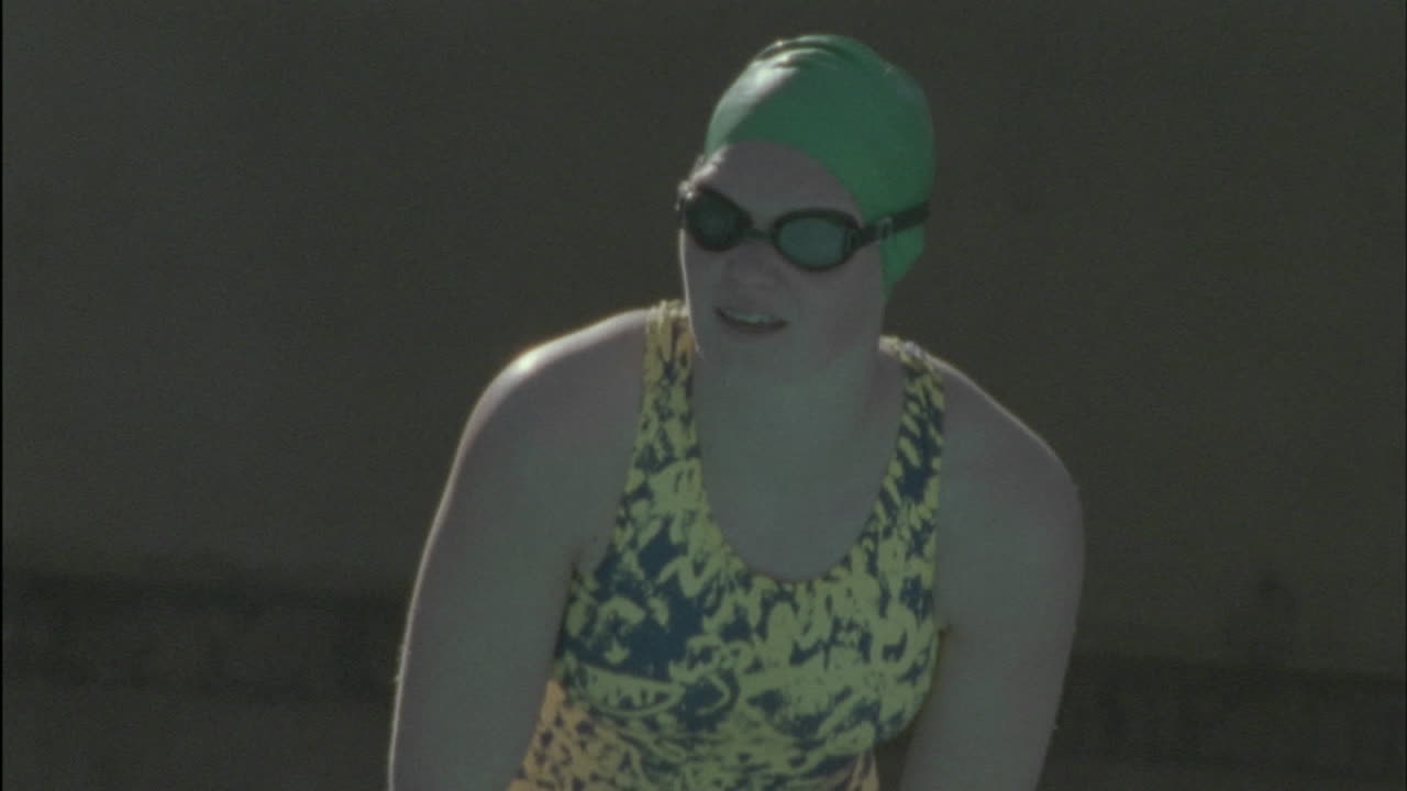 한 여자가 몸을 숙이고 수영장으로 뛰어들어 헤엄치기 시작합니다.