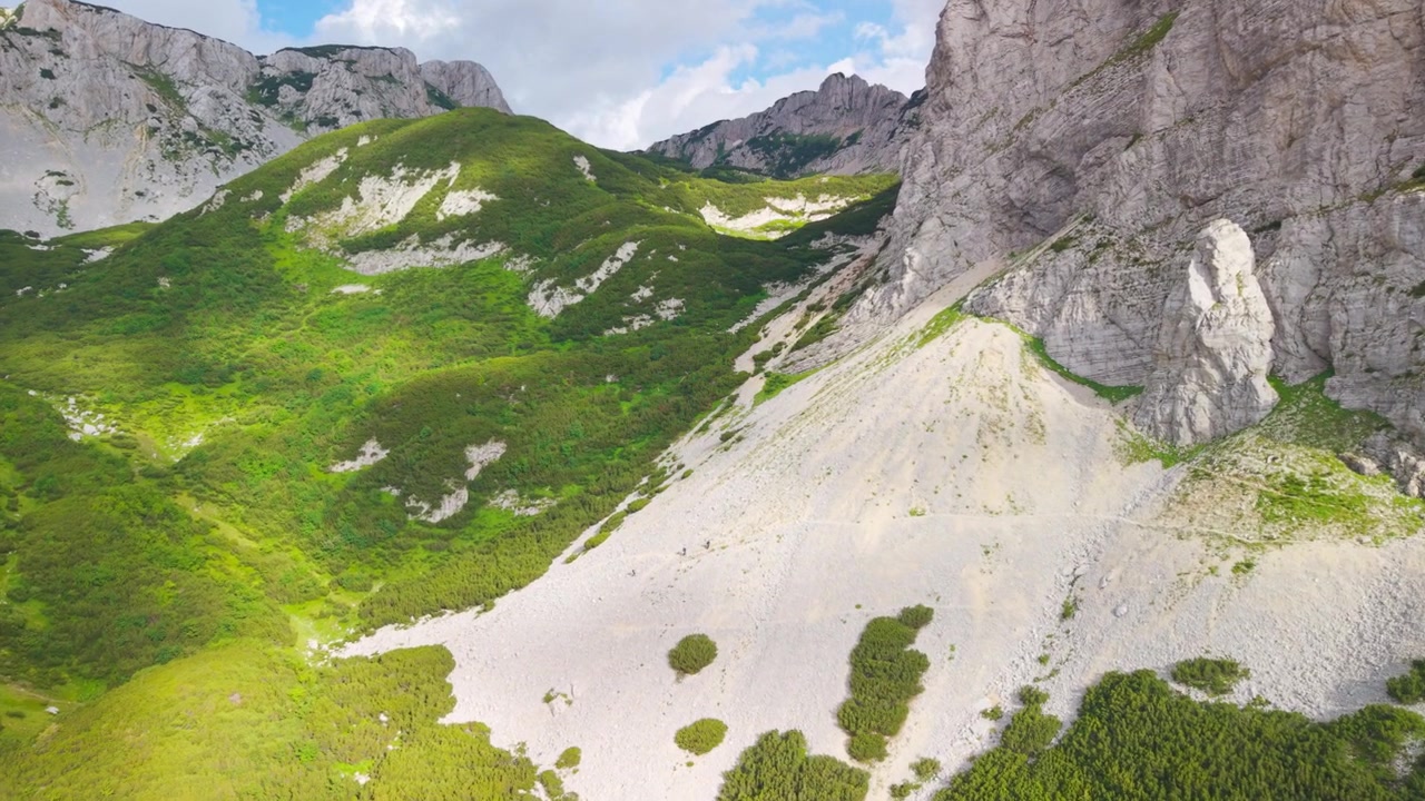 Escursionisti che attraversano un sentiero di ghiaione lungo imponenti scogliere calcaree all'avvicinamento al Lago Skrcko, Parco Nazionale del Durmitor, Montenegro.