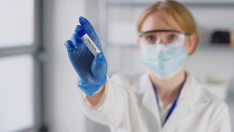 trabajadora de investigación de laboratorio con gafas de seguridad y máscara sosteniendo un tubo de ensayo etiquetado omicron