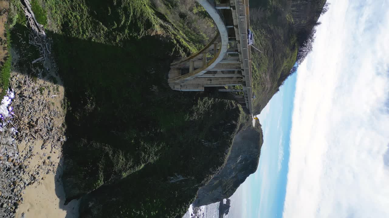 Young woman overlooks the ocean and a bridge from the edge of a cliff