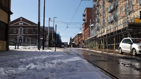 Car-driving-on-sunny,-snowy,-city-street-near-tramlines,-Sheffield,-low-angle