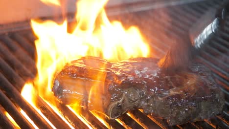 close-up of flipping a juicy steak on the bbq and brushing on sauce as the flames rise on the grill