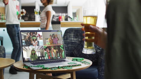 persona en un bar usando una computadora portátil haciendo una videollamada del día de san patricio con amigos en otro bar