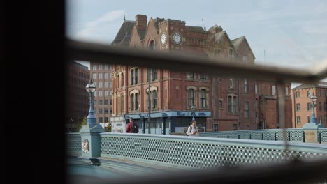 urban commuters walk across city bridge, viewed through railing, with soft daylight and steady camera