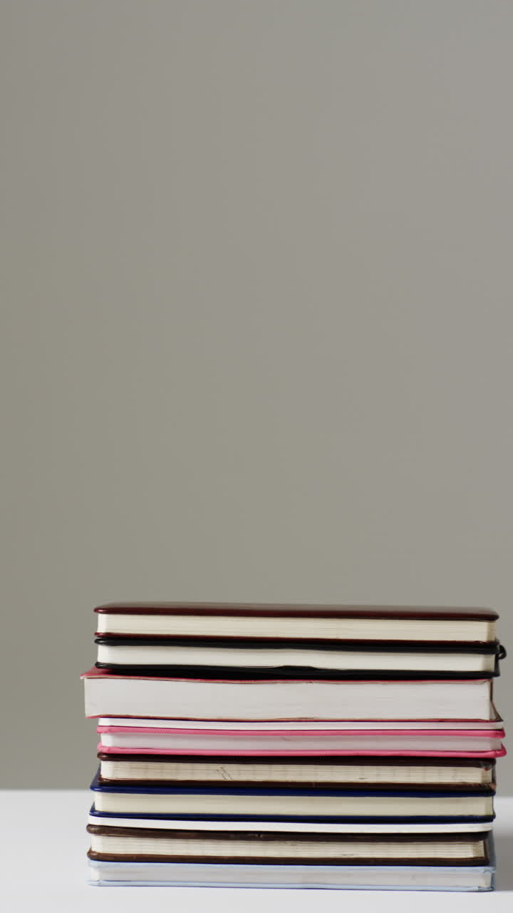 Vertical video of stack of books with copy space on grey background, in slow motion