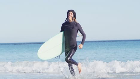 video of smiling caucasian man with dreadlocks in wetsuit carrying surfboard running out of sea