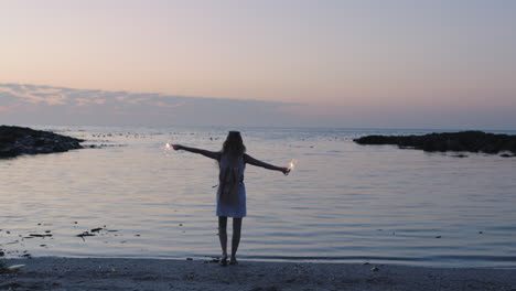 Porträt-Einer-Jungen-Frau-Mit-Erhobenen-Wunderkerzen,-Die-Am-Friedlichen-Strand-Spaziert-Und-Abenteuer-Feiert