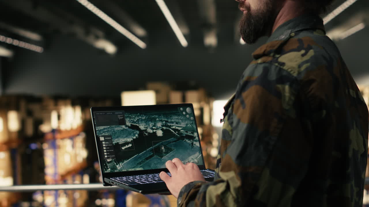 Man in Camouflage Jacket Operating Laptop in Warehouse