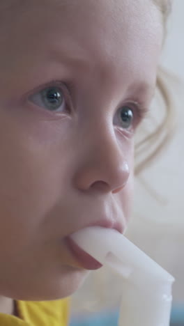 tired little girl in yellow shirt undergoes medical procedure with inhaler in light room extreme close view