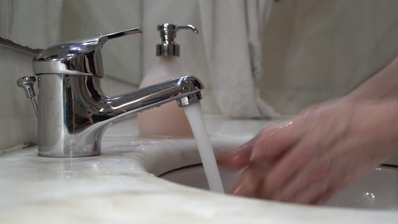 young man's hand's are washed on tap water with liquid soap, then rinsed and wiped on a white cloth towel - side view close-up static shot 4k