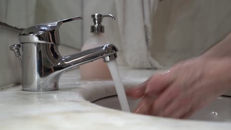 young-man's-hand's-are-washed-on-tap-water-with-liquid-soap,-then-rinsed-and-wiped-on-a-white-cloth-towel---side-view-close-up-static-shot-4k