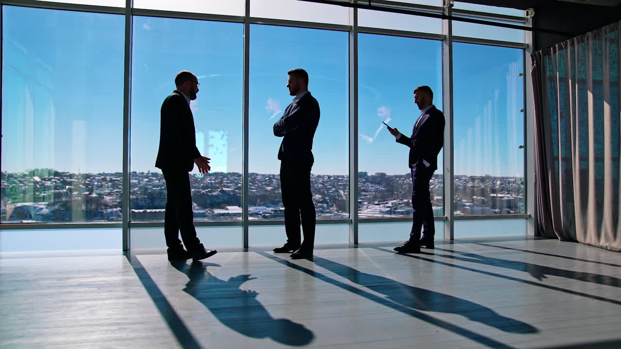 Male entrepreneurs during break. Business people standing near office windows and having pleasant conversation.