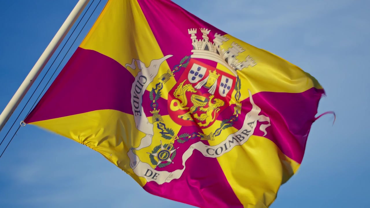 Primer plano en cámara lenta de la vibrante bandera de Coimbra ondeando al viento contra un cielo azul brillante.