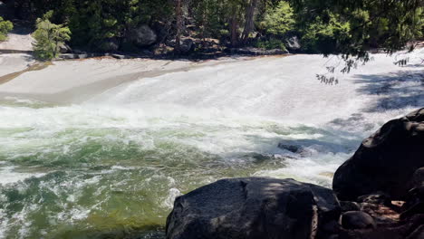 a calm corner of water pans up to a long flat waterfall in yosemite national park