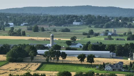 american farm fields and farmsteads with barn in rural area. sunny day in summer season. aerial wide shot. green trees avenue and silo storage for grain and food
