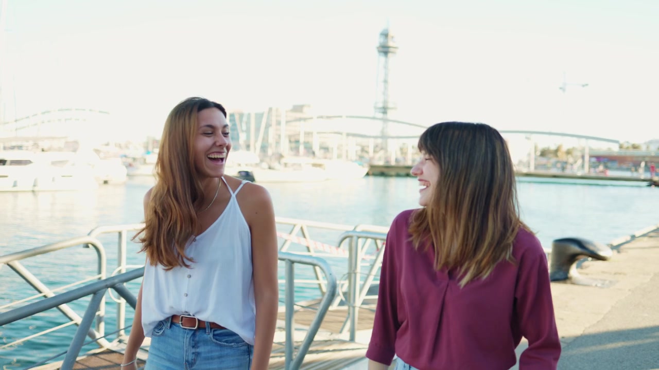 Zwei junge Frauen spazieren und lachen auf einem Hafensteg