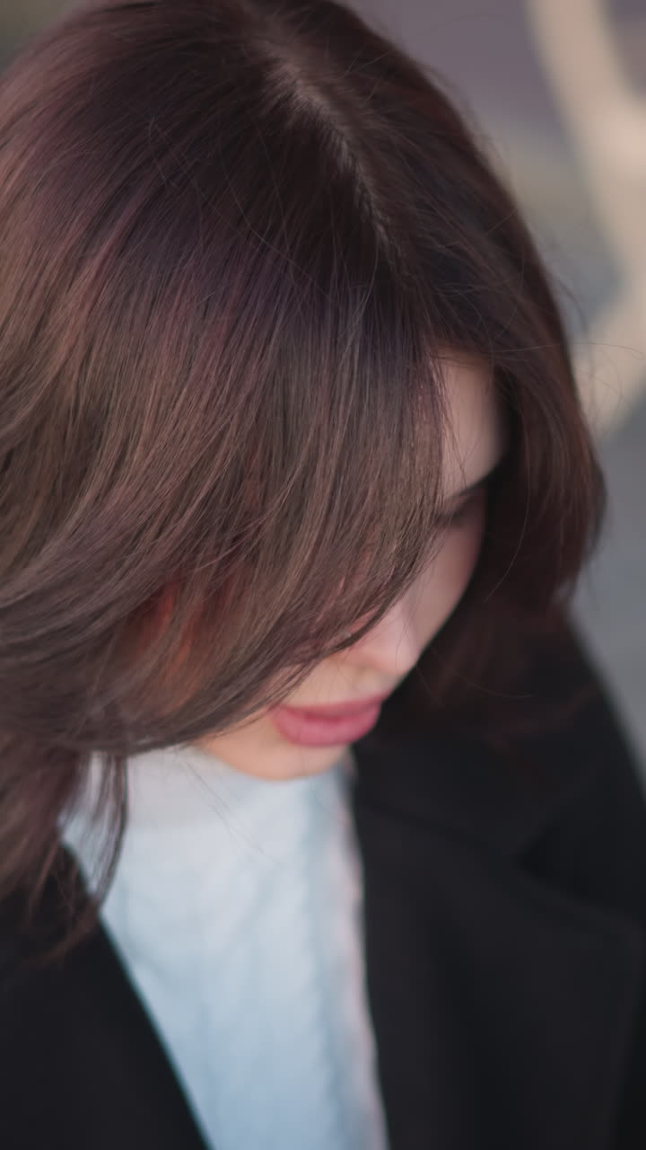 밖에서 앉아있는 어린 소녀, 그녀의 앞에 있는 무언가에 초점을 맞추고, 그녀는 그녀의 머리를 조정, 배경에 나무 의자와 기둥의 흐릿함