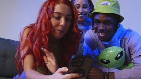 fotografía de estudio de cerca de amigos jóvenes de la generación z sentados en el sofá compartiendo publicaciones en las redes sociales en teléfonos móviles 4