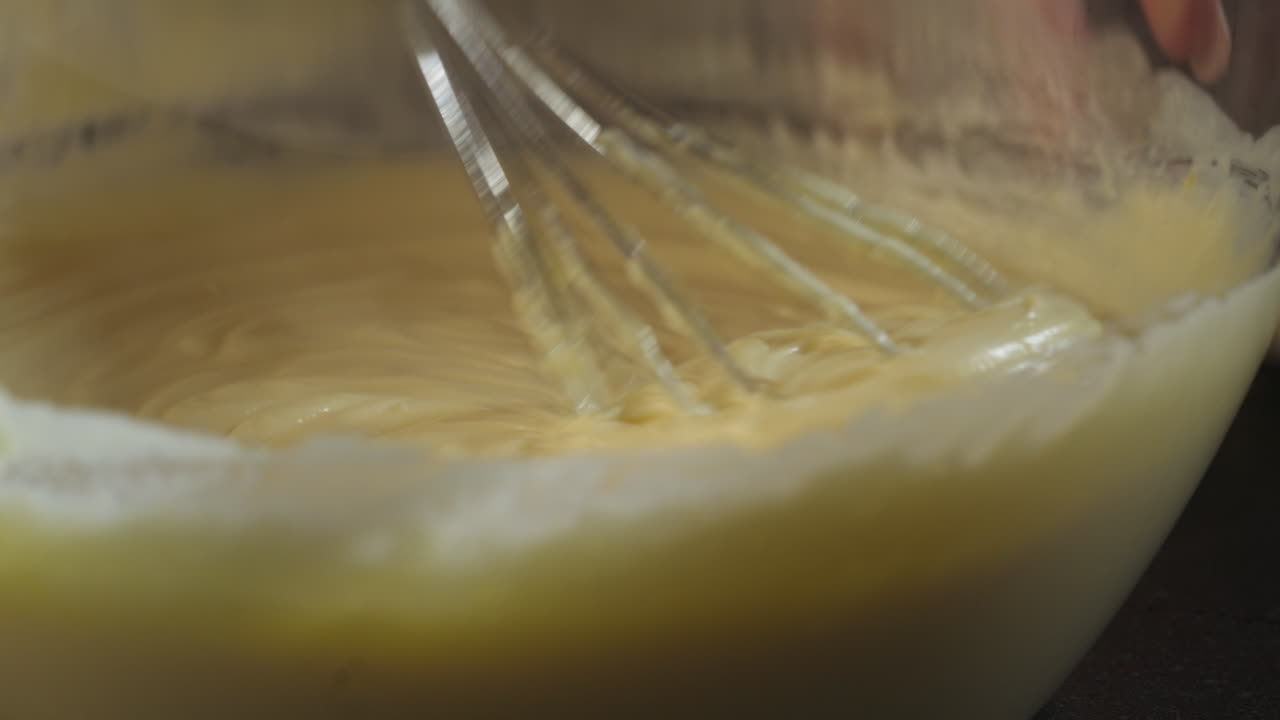 Person stirring tiramisu dough in a glass bowl with a hand mixer