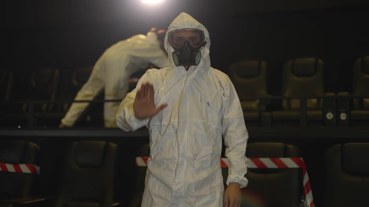 Un uomo che mostra il segnale di stop - in piedi nel cinema vuoto, con indosso una tuta protettiva bianca