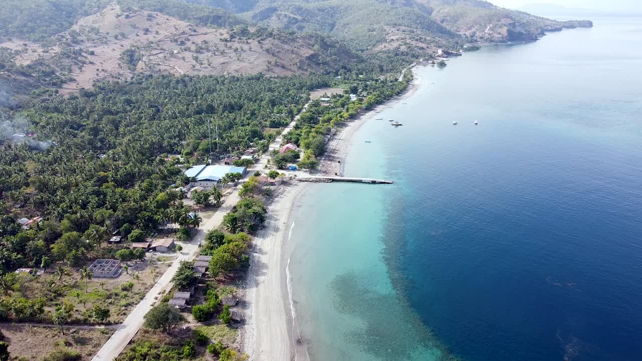 Rugged mountain shoreline with white sandy beach and turquoise ocean and coral reefs on remote tropical island, Atauro Island in Timor Leste, static aerial drone