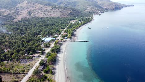 rugged mountain shoreline with white sandy beach and turquoise ocean and coral reefs on remote tropical island, atauro island in timor leste, static aerial drone