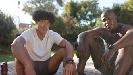 smiling multiracial male friends sitting outdoors, relaxing and enjoying time together in sunlight