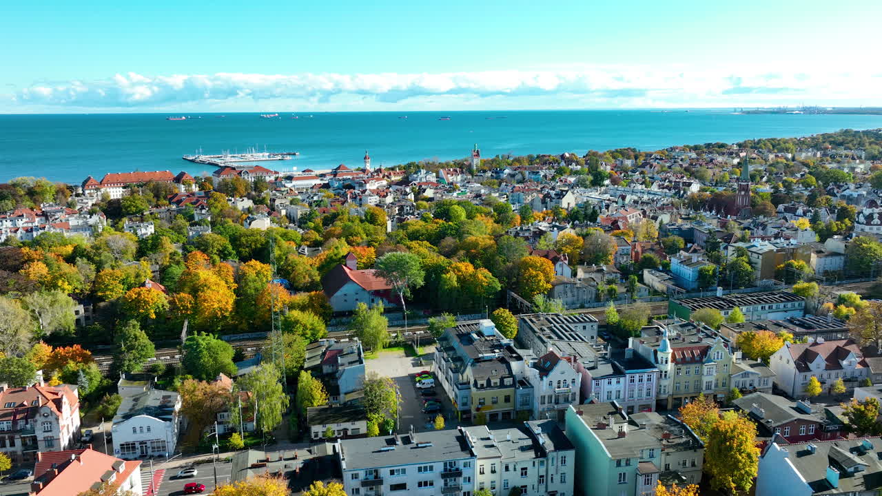 Wide aerial drone shot of Sopot residential area with colorful autumn trees, stretching to the sea and marina on a sunny day