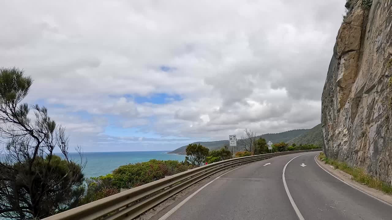 A coastal drive showcasing ocean views, cliffs, and lush greenery under a partly cloudy sky