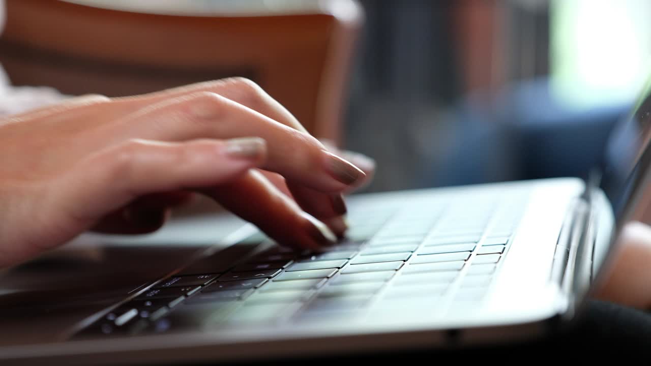 las manos de una mujer trabajando y escribiendo en el teclado de la computadora portátil en la mesa