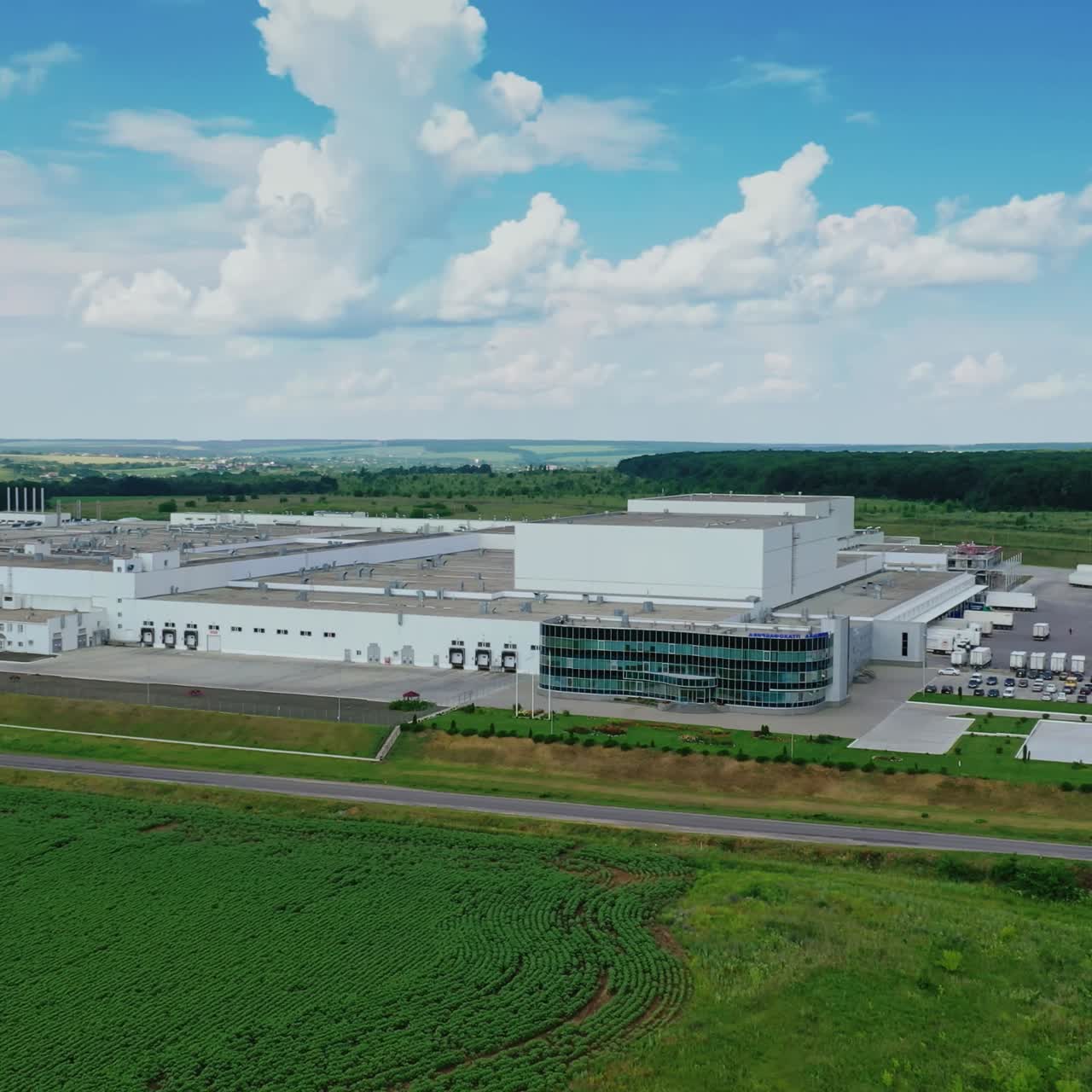 Modern manufacture in nature. Huge industrial complex among picturesque green field. Large factory under blue sky. Aerial view.