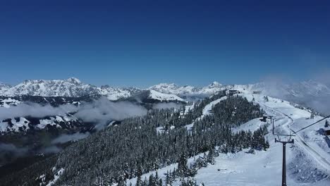 Snowy-ski-resort-with-pine-trees,-clouds-in-the-valleys