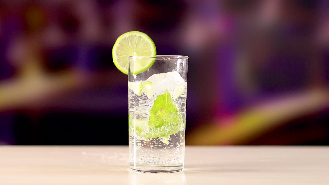 A mojito cocktail with lime and mint on a wooden surface, set against a blurred, colorful background