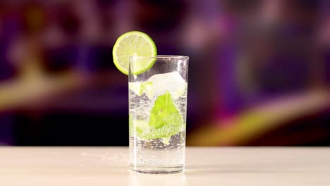 a mojito cocktail with lime and mint on a wooden surface, set against a blurred, colorful background
