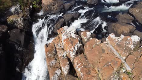 Aerial-view-over-a-river-flowing-through-sharp-rocks,-in-Drakensberg-Mountain-Range,-South-Africa