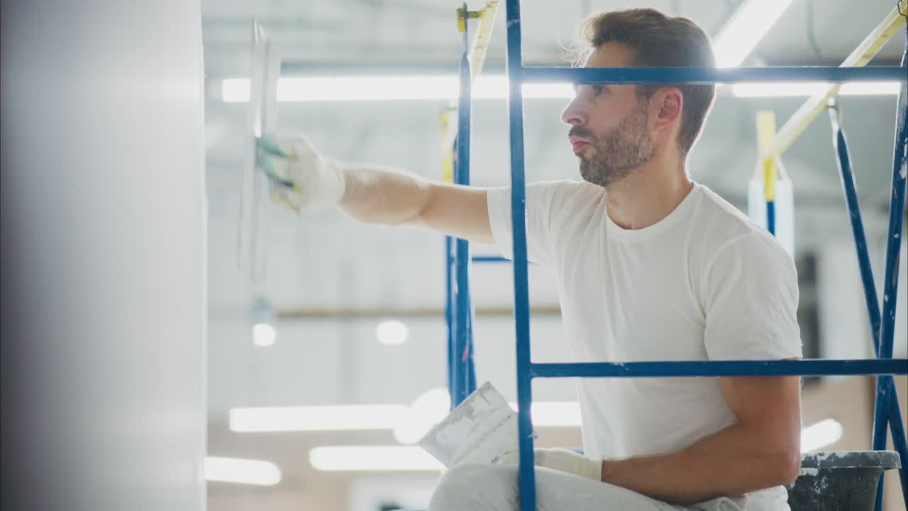 Skilled Worker Applying Finishing Touches to Wall while Working on Scaffolding in Brightly Lit Space, Showcasing Craftsmanship and Attention to Detail
