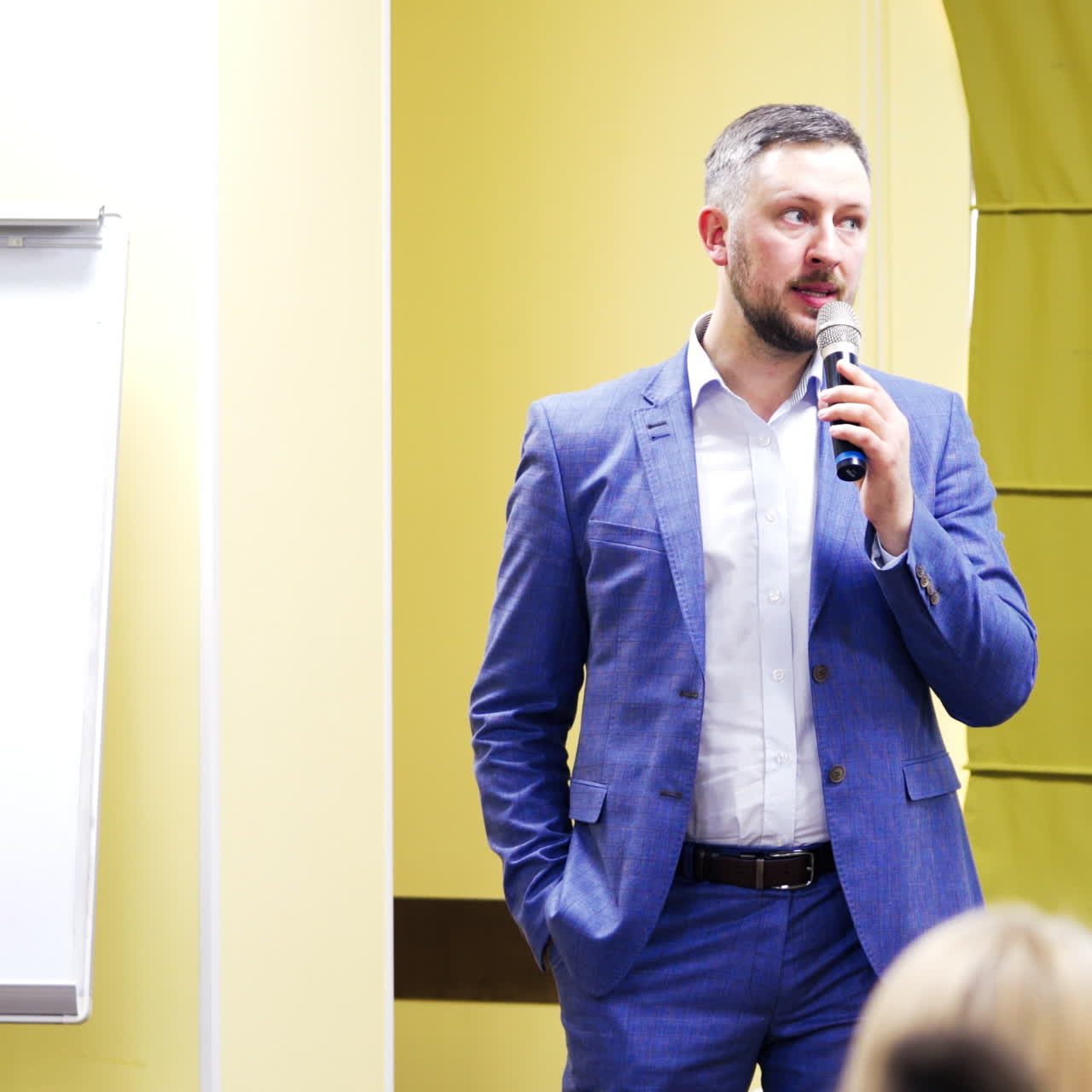 Professional confident executive manager with microphone speaking at symposium for the public. Businessman gives advices for audience during business forum.