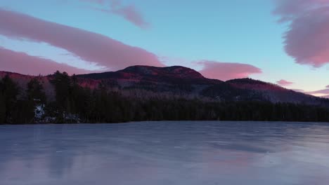 Aerial footage flying low acrosse the surface of a frozen pond towards a mountain lit by sunrise