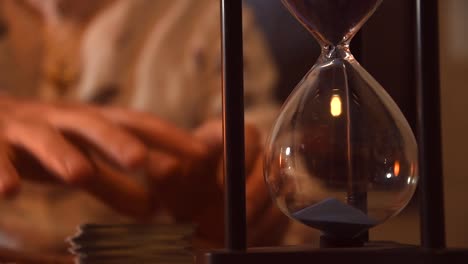 hourglass marking the time with its blue sand, with a man using tarot cards in the background