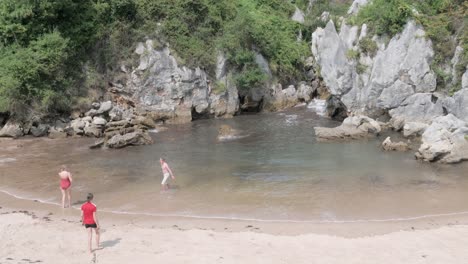 two people playing paddleball at playa de gulpiyuri, the smallest inland beach in the world, surrounded by green cliffs and clear waters