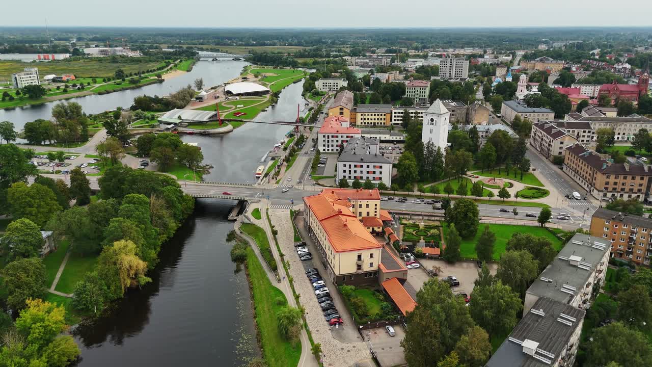 Drone footage of Jelgava city in Latvia with the Lielupe River, Jelgava Palace, bridge, and Mītava concert hall visible in the urban landscape