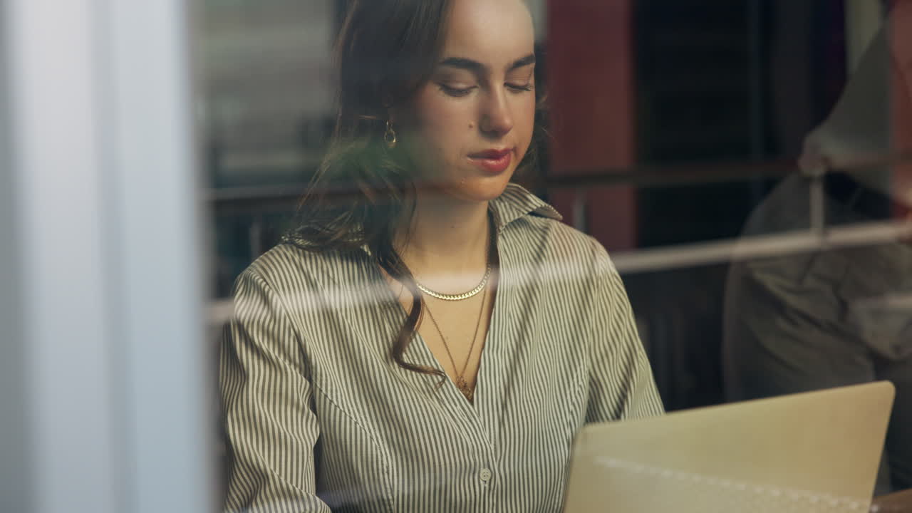 A young woman works on her laptop in an indoor setting